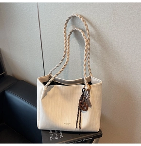 Detail of woven tote bag featuring braided handles and decorative brown hanging charms