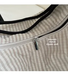 Close-up of smooth silver metal zipper on beige striped polyester hobo bag detail