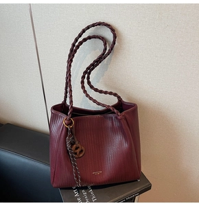 Macro detail of burgundy tote bag showing woven texture and round logo pendant charm