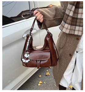 Détail du sac cabas en cuir marron foncé avec poche à boucle et charm chiot en tricot