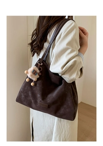 Deep brown matte suede tote bag shown on shoulder with cute plush lion charm detail