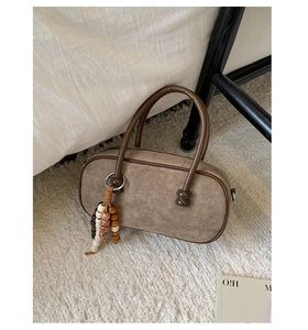 Dettaglio borsa Boston scamosciata marrone con ciondolo etnico su tappeto morbido