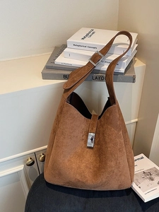 Brown suede tote bag with adjustable wide strap and metallic buckle in a minimalist setting