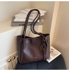 Detail of coffee brown woven tote bag featuring a pretzel charm and braided handle