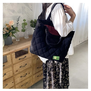 Detail view of black quilted tote bag featuring a green designer label and soft菱格纹 texture