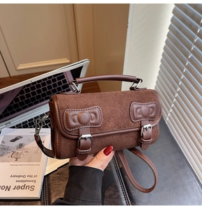 Detail of brown suede crossbody bag with leather bow accents and silver metal buckles
