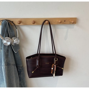 Detail of dark brown woven tote bag featuring golden logo and ethnic style bead ornament