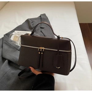 Detailed view of dark brown crossbody bag with gold zippers on a grey blazer background