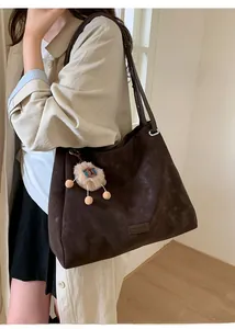 Detail of dark brown suede tote bag featuring a lion plush charm and long shoulder strap