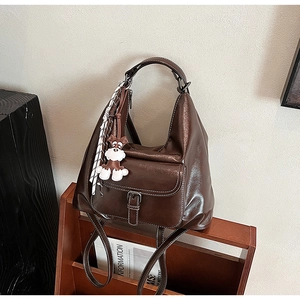 Détail d'un sac cabas marron foncé effet vintage avec breloque chien sur étagère en bois
