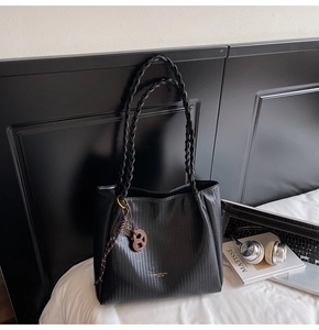Detail of black woven texture tote bag with golden metal hardware and round pendant charm