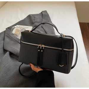 Detail of minimalist black leather handbag with golden dual zippers and elegant fringe tassel