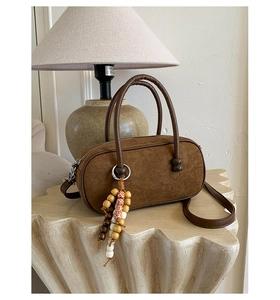 Dettaglio borsa bowling in camoscio marrone con ciondolo boho su base crema