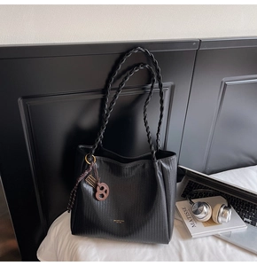 Detail of black woven tote bag with metallic abacus charm on white bedding setup