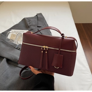 Detail view of burgundy handbag featuring smooth leather and intricate woven texture