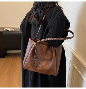 Close-up of brown tote bag featuring woven texture, thick braided strap and tassel detail