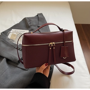 Close-up of burgundy leather handbag with woven pattern and dual gold zippers detail