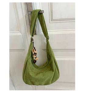 Gros plan du sac hobo en daim vert avec un pendentif vintage en perles sur la bandoulière