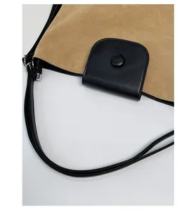 Detail of beige suede shoulder bag featuring a black leather flap and silver metal ring