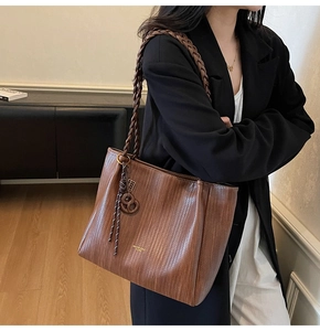 Close-up of dark brown woven leather tote bag featuring chunky shoulder strap and charm