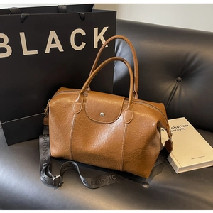 Detail of a brown leather Boston bag featuring a vintage pebble texture and wide woven strap