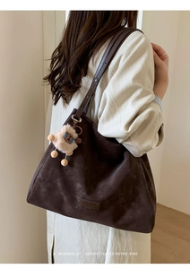 Detail of dark brown faux suede tote bag with a cute plush lion charm and logo plate