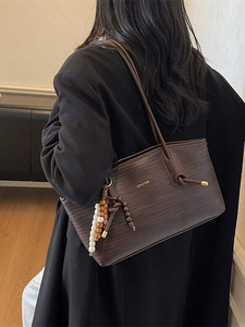 Deep brown woven shoulder tote bag with gold lettering and colorful beaded charm