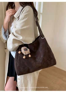 Detail of dark brown matte tote bag featuring a cute plush lion charm and shoulder strap