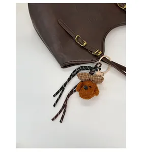 Detail eines süßen Plüschwelpen-Anhängers mit Karoschleife an brauner Ledertasche
