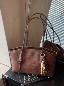 Brown woven tote bag with shoulder straps and decorative beads on a modern shelf