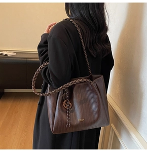 Detail of coffee brown woven tote bag with wide braided strap and metallic gold charm