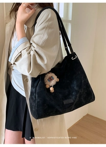 Close-up of black matte tote bag with thin shoulder straps and a plush bear pendant