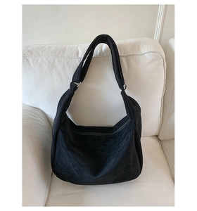 Sac hobo noir minimaliste en daim avec bandoulière large sur un canapé blanc