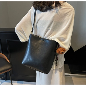 Side view of a black leather bucket bag with a cute plush bear charm on a model