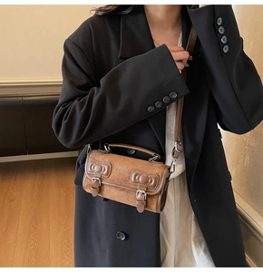 Close-up of deep brown suede handbag with decorative bow relief and dual buckle straps