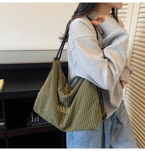 Detail view of a green plaid tote bag with FASHION embroidery and soft shoulder strap