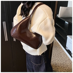 Vue détaillée du sac à bandoulière marron foncé brillant porté par un mannequin chic