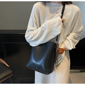 Detail of minimalist black leather bucket bag with a cute brown teddy bear keychain
