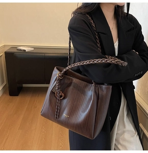 Detail of dark brown tote bag with woven texture and braided handle for commuting