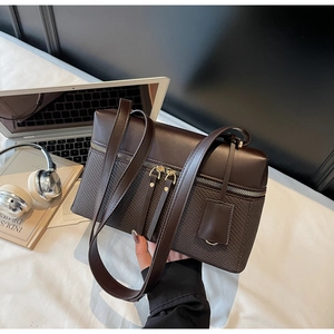Close-up of brown patchwork shoulder bag with dual zippers and woven texture in city setting