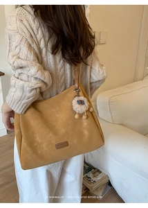 Close-up of brown suede tote bag with brand label and cute plush sheep charm