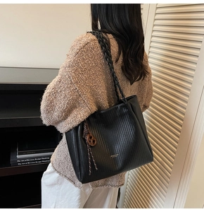 Detail of black woven texture tote bag with braided double straps and round pendant