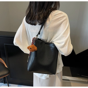 Detail of black leather bucket bag on shoulder with a cute brown teddy bear keychain
