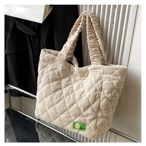 Detail of quilted corduroy tote bag in cream with a ruched handle and green logo label