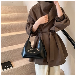 Sac hobo en cuir noir brillant porté avec un trench marron dans un décor de studio