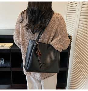 Detail of a black woven tote bag with a thick strap and ribbon charm on a model