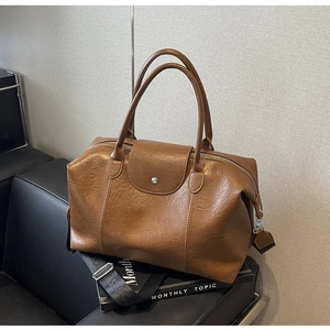 Detail view of brown Boston bag with ruched faux leather texture and a fabric strap