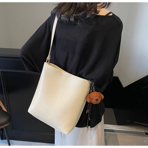 Detail view of cream white litchi pattern leather tote bag with brown plush bear charm