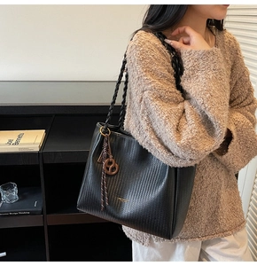 Detail of black woven tote bag with round leather charm and dual braided handles
