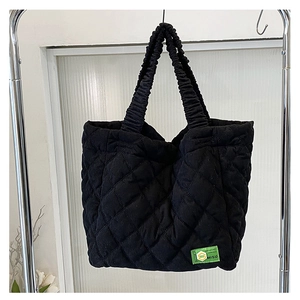 Detail of black quilted handbag featuring a ruched handle and green MISU woven label